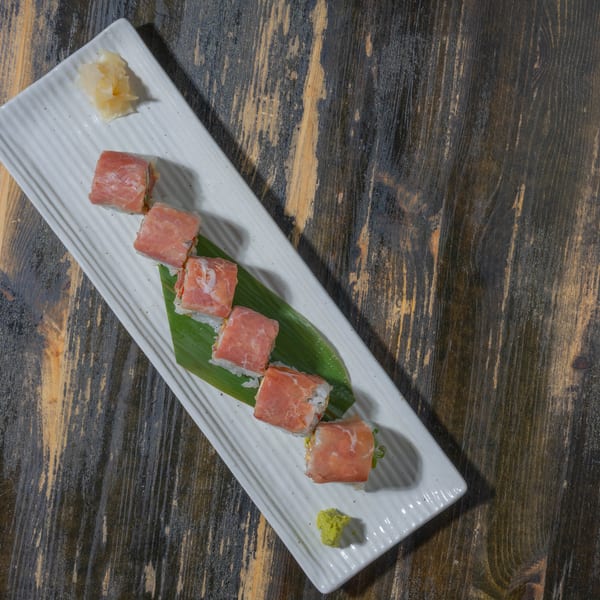 Sushi rolls wrapped in thinly sliced meat, with ginger and wasabi, on a white rectangular plate.