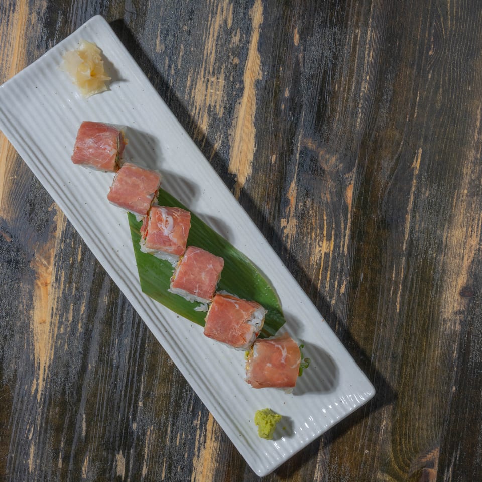 Sushi rolls wrapped in thinly sliced meat, with ginger and wasabi, on a white rectangular plate.