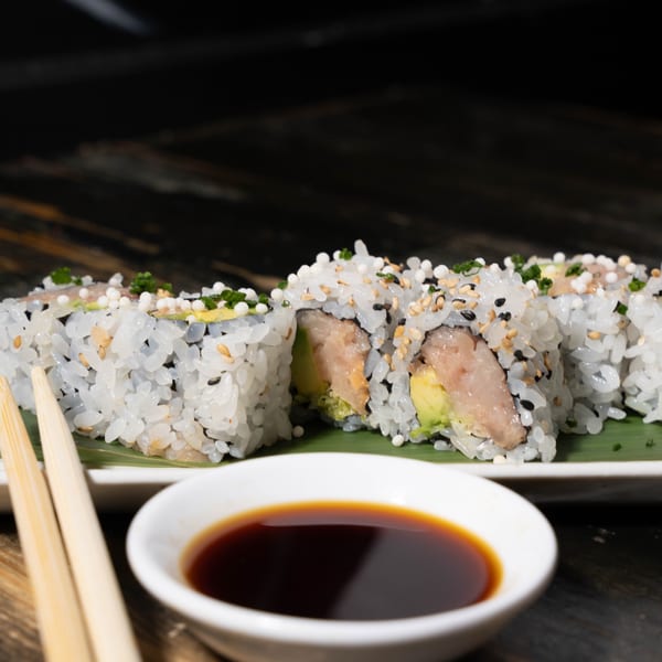Sushi rolls with white rice, sesame seeds, and avocado, served with chopsticks and soy sauce.