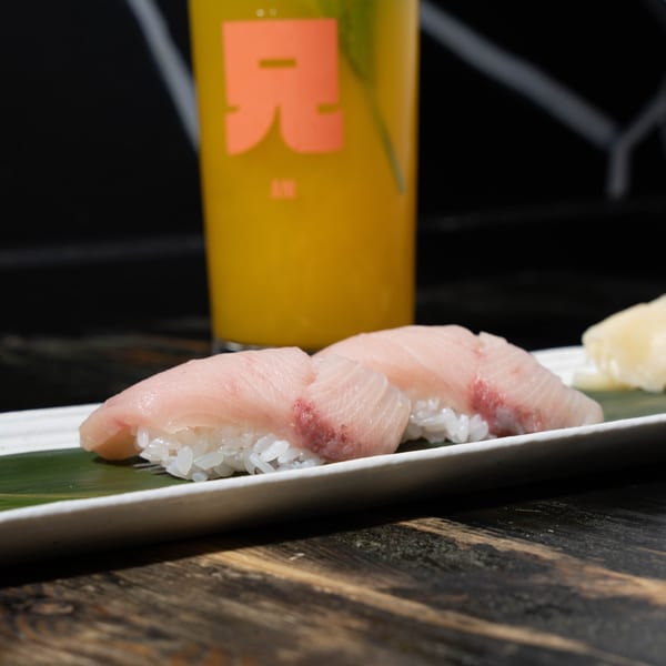 Two pieces of nigiri sushi with light pink fish on rice, served with a yellow drink.