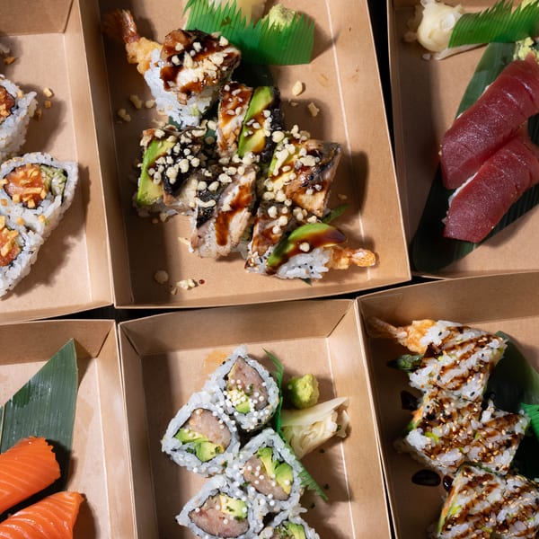 Assorted sushi rolls and sashimi in six brown takeout containers, viewed from above.