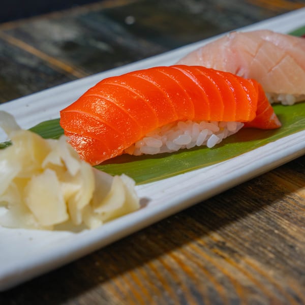 Two pieces of nigiri sushi, salmon and white fish, with pickled ginger on a white plate.