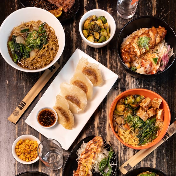 A variety of Japanese dishes, including ramen, rice bowls, dumplings, and grilled meats, on a dark wooden table.