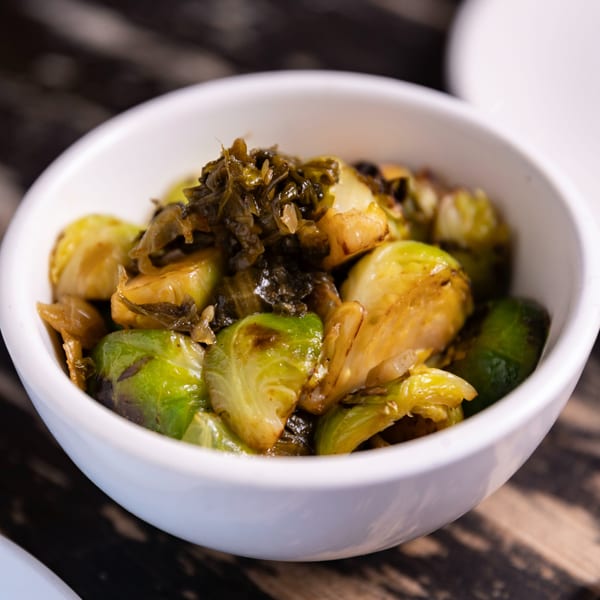 A white bowl filled with roasted Brussels sprouts and dark green relish on a wooden table.
