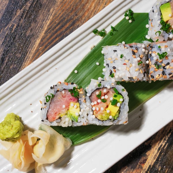 Sushi rolls with tuna, avocado, and roe on a white plate with wasabi and ginger.