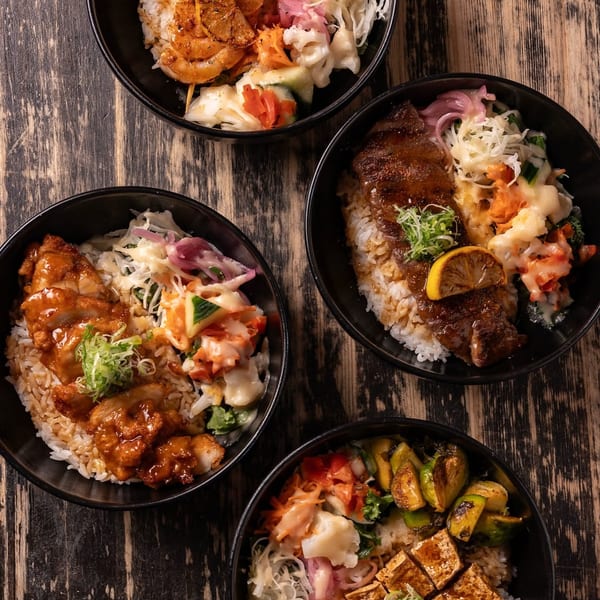 Four colorful rice bowls with shrimp, steak, chicken, and tofu, on a rustic wooden table.