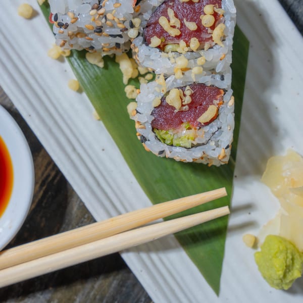 Tuna sushi rolls with sesame seeds, tempura flakes, soy sauce, chopsticks, ginger, and wasabi.