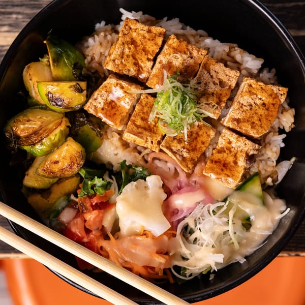 A black bowl filled with rice, tofu, roasted brussels sprouts, and various pickled vegetables.
