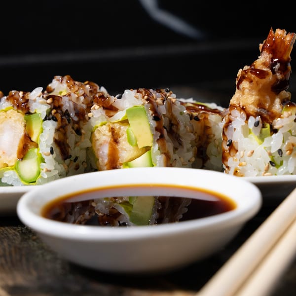 Tempura shrimp sushi rolls with avocado, sesame seeds, and eel sauce, with a side of soy sauce.