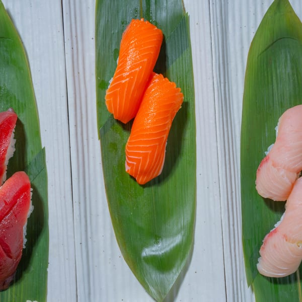Three pairs of sushi, tuna, salmon, and yellowtail, presented on green leaves on white plates.