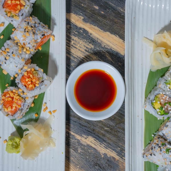 Two plates of sushi rolls with salmon, avocado, and various toppings, served with soy sauce, wasabi, and ginger.