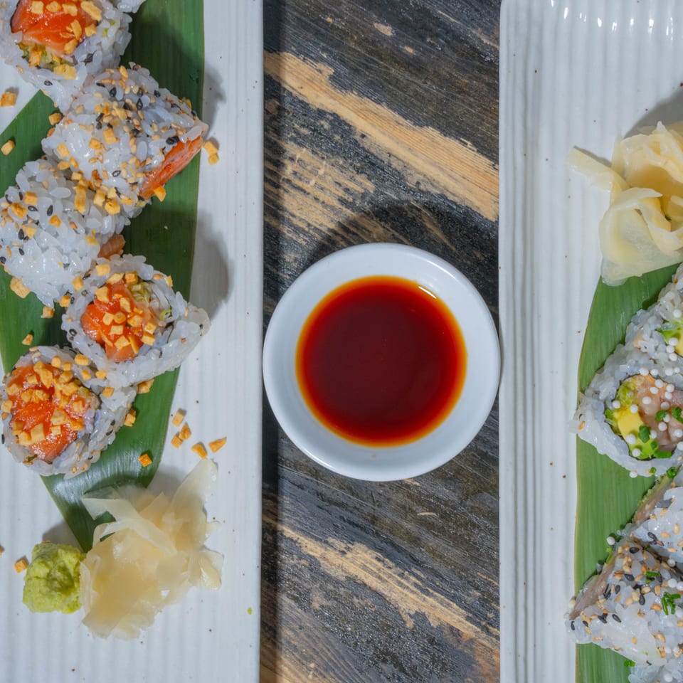 Two plates of sushi rolls with salmon, avocado, and various toppings, served with soy sauce, wasabi, and ginger.
