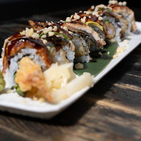 Dragon roll sushi with eel, avocado, and tempura flakes, served with ginger and wasabi.