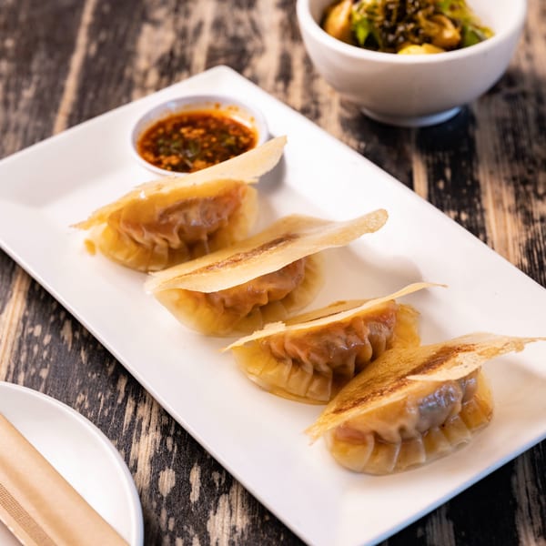 Four pan-fried dumplings with crispy edges and a side of chili oil on a white plate.